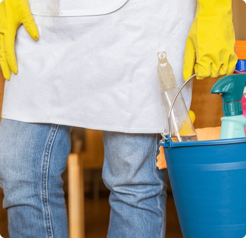 Person wearing yellow gloves holding a blue bucket with cleaning supplies.
